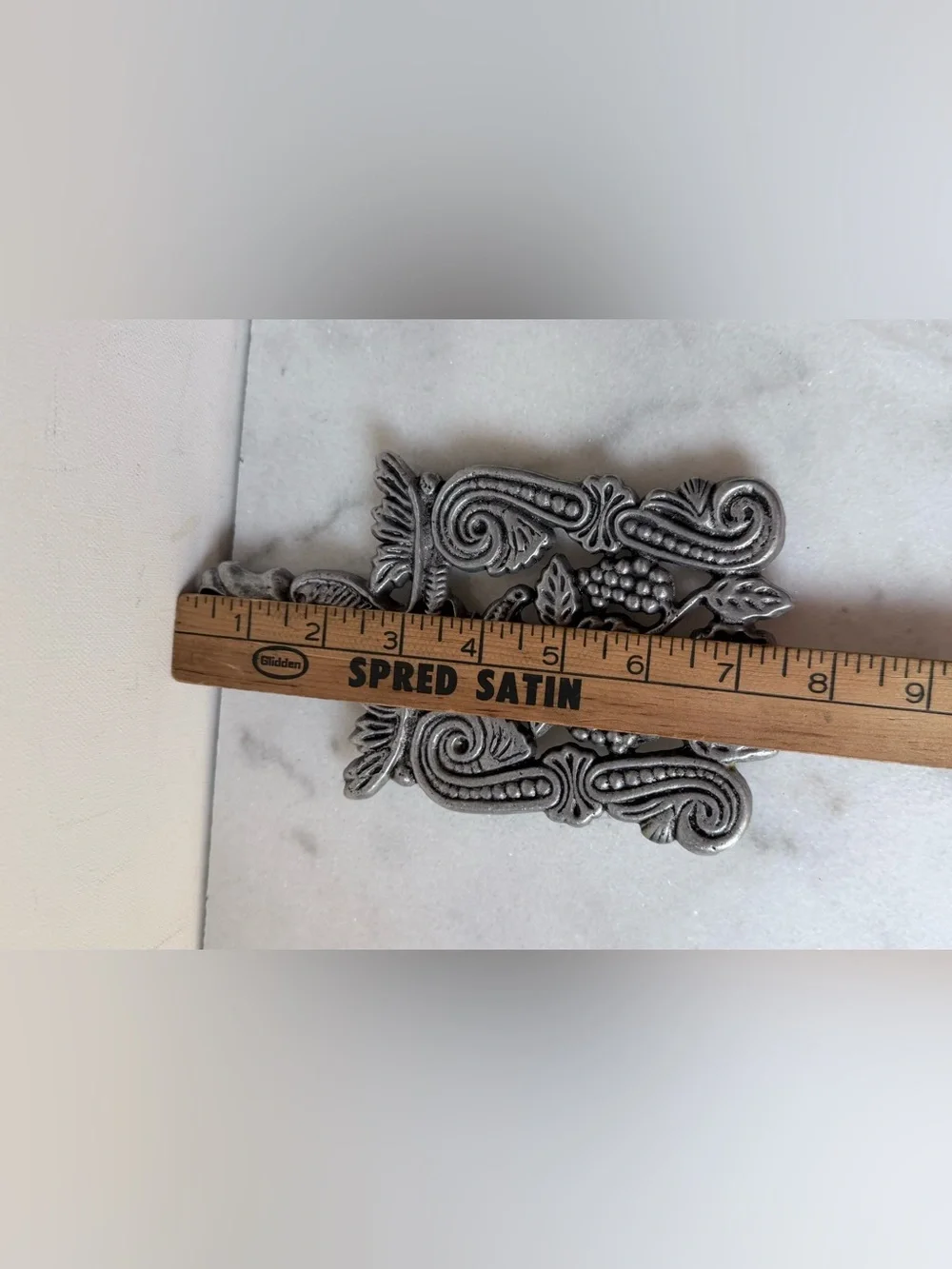 vintage silver-toned metal trivet featuring a decorative design grapes scrolls.